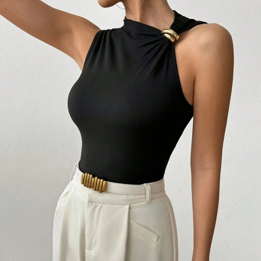 Person wearing a black sleeveless top with gold accents and white pants on a plain background